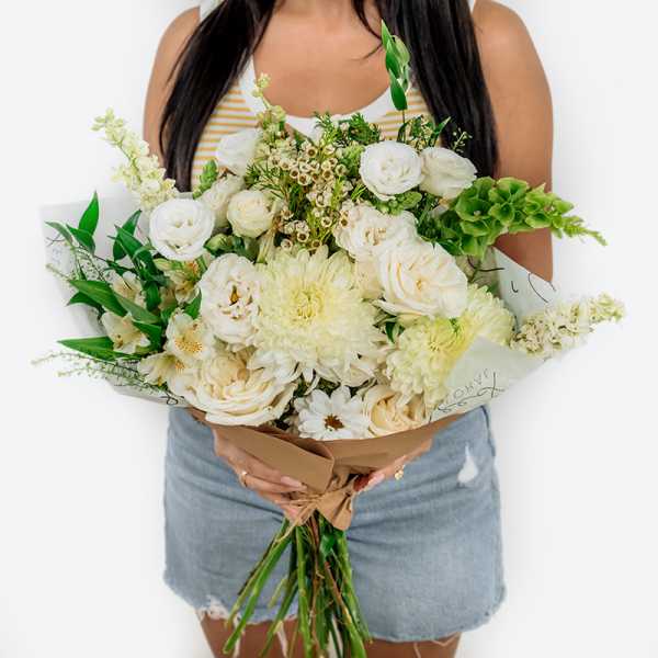 Large bouquet of white flowers with green accents wrapped in brown paper