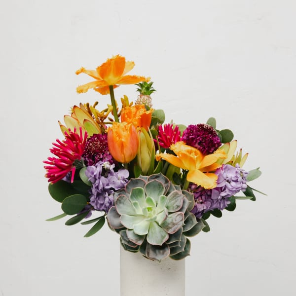 Colorful bouquet with succulents, orange tulips, and purple blooms in a white vase
