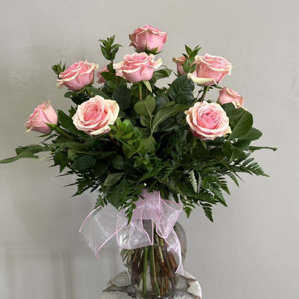 Pink roses arranged in a clear glass vase with a pink ribbon bow