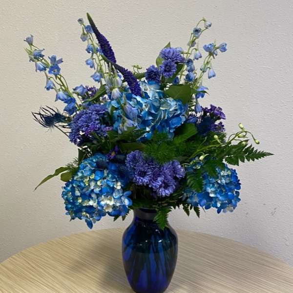 Blue and purple flower arrangement in a dark glass vase