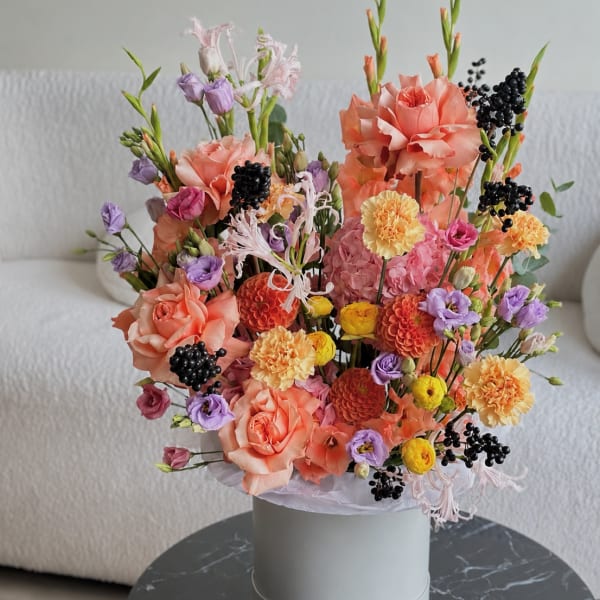 Mixed bouquet of peach, pink, purple, and yellow flowers in a white hat box