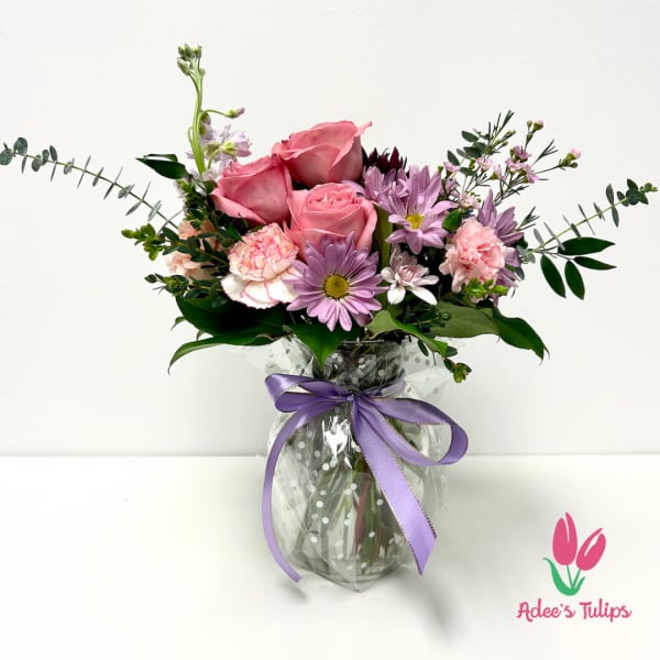 Pink roses and lavender daisies in a glass vase with a purple ribbon