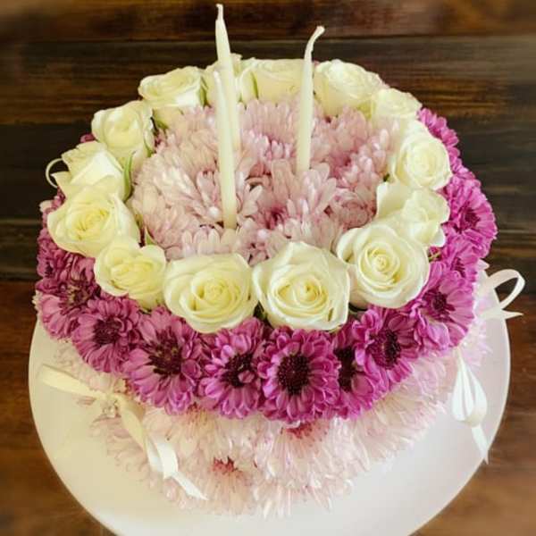 Round floral cake with white roses, pink daisies, and two candles