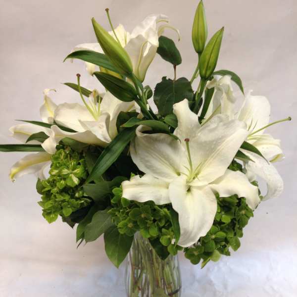 White lilies arranged in a clear glass vase with green blooms