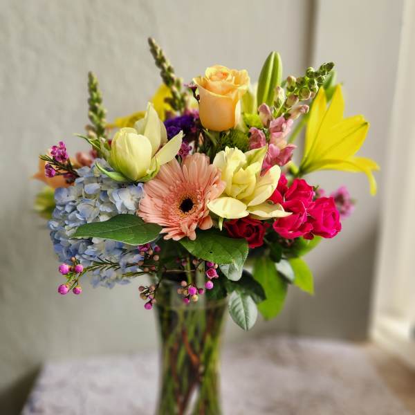 Mixed bouquet in a clear glass vase with roses, gerbera daisy, hydrangea, and lilies