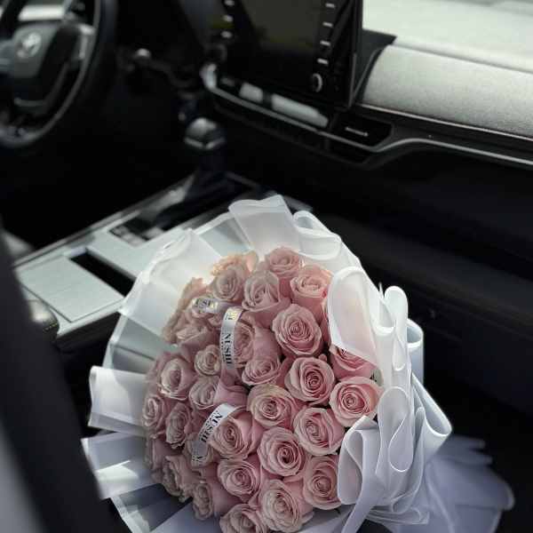 Bouquet of pale pink roses wrapped in white paper and ribbon on a car seat