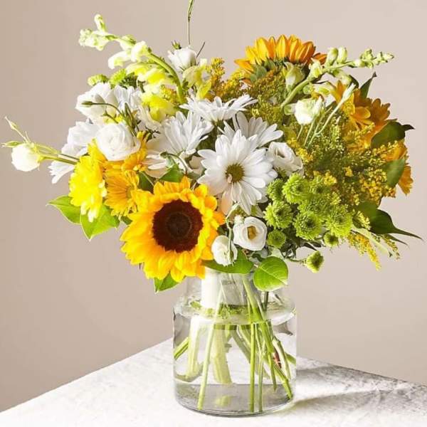 Bouquet of sunflowers, white daisies, and yellow flowers in a glass vase