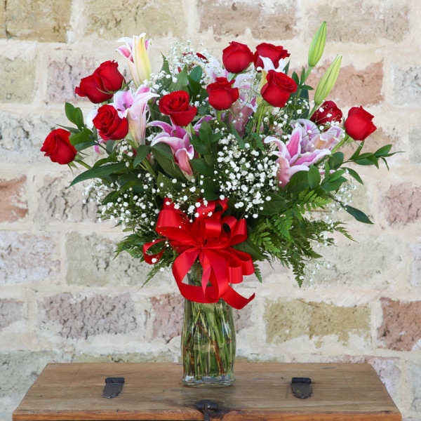 Bouquet of red roses and pink lilies in a glass vase with a red ribbon
