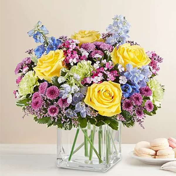 Yellow roses and pastel mixed flowers in a clear square vase