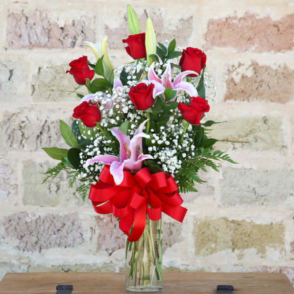 Bouquet of red roses and pink lilies in a clear glass vase with a red bow