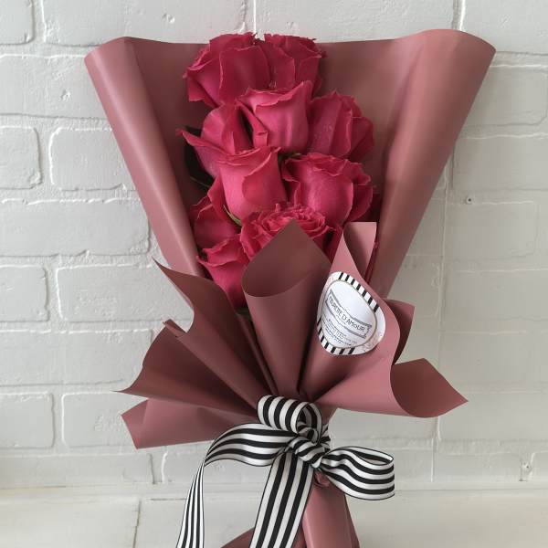 Bouquet of hot pink roses wrapped in dusty pink paper with a striped ribbon