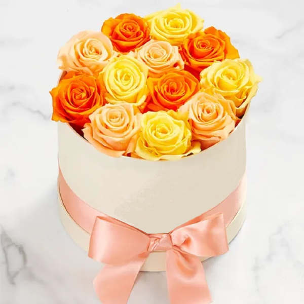 Round box of yellow, peach, and orange roses with a pink ribbon
