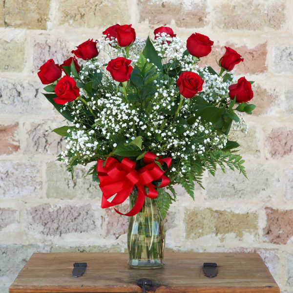 Red roses and baby's breath in a glass vase with a red ribbon