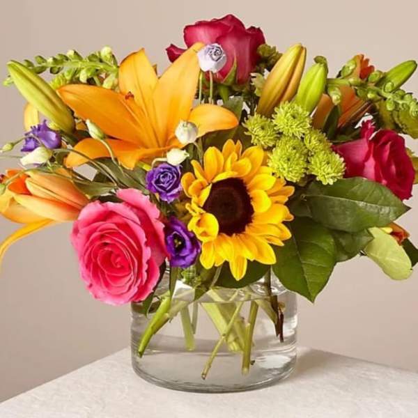 Mixed bouquet of roses, lilies, and a sunflower in a glass vase