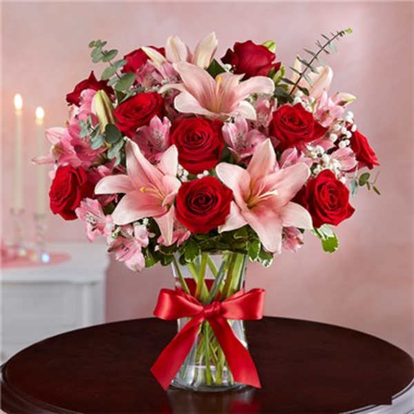 Bouquet of red roses and pink lilies in a glass vase with a red ribbon