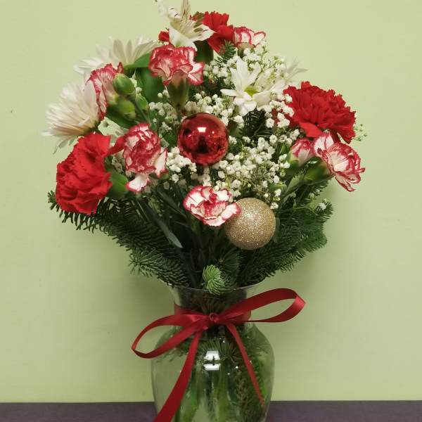 Red and white floral arrangement in a glass vase with holiday ornaments