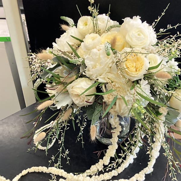 Cream and white floral arrangement in a glass vase with trailing accents