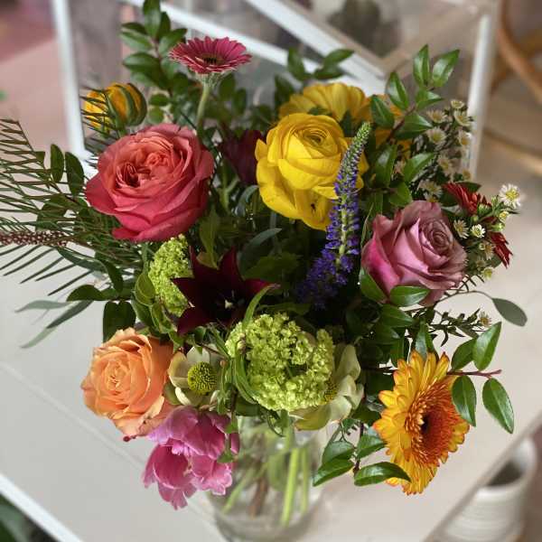 Mixed bouquet of colorful roses, gerbera daisies, and other blooms in a glass vase