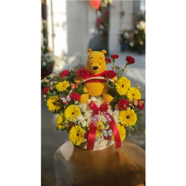 Basket arrangement with a Winnie the Pooh plush surrounded by yellow and red flowers