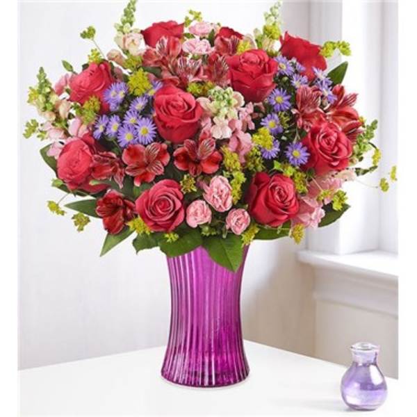 Mixed bouquet of red roses and purple daisies in a pink vase
