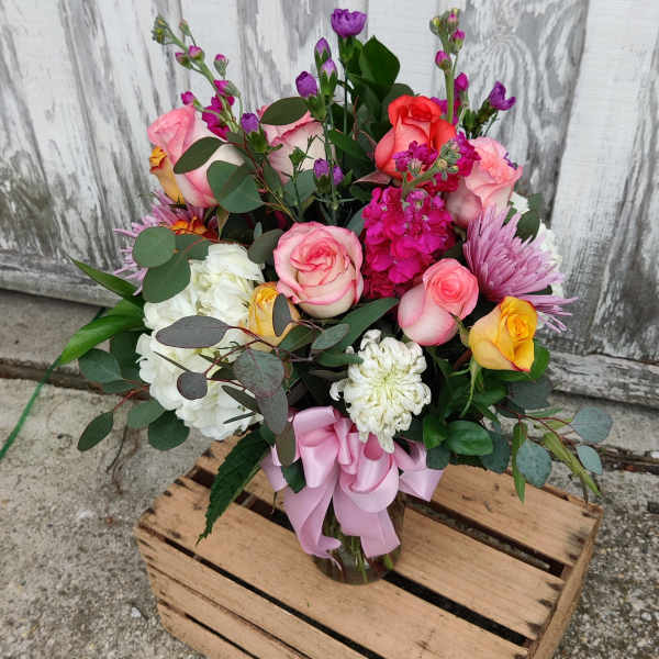 Mixed bouquet of pink, white, yellow, and purple flowers in a glass vase with a pink ribbon
