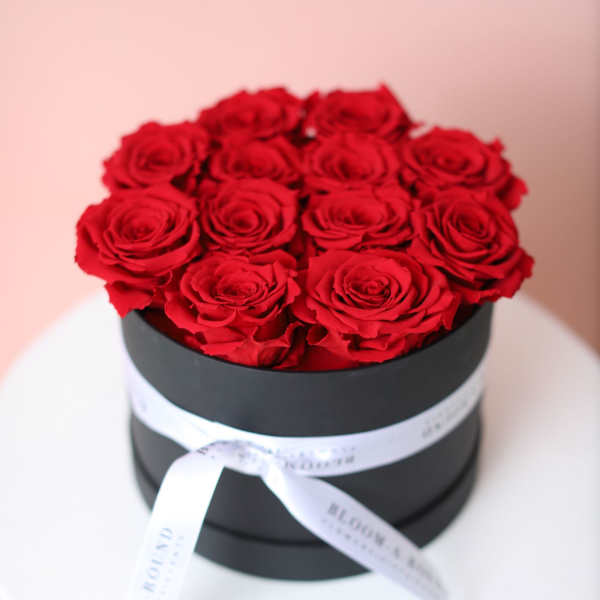 Red roses arranged in a black round box with a white ribbon
