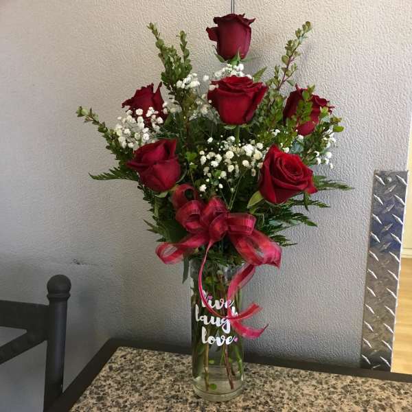 Red roses arranged in a clear glass vase with a pink ribbon