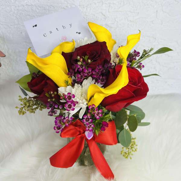 Bouquet of red roses, yellow calla lilies, and white flowers with a red ribbon