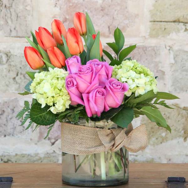 Pink roses and orange tulips in a glass vase with burlap ribbon