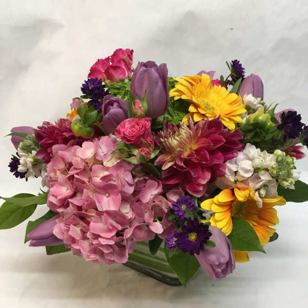 Mixed bouquet with pink hydrangea, purple tulips, and yellow daisies in a glass vase