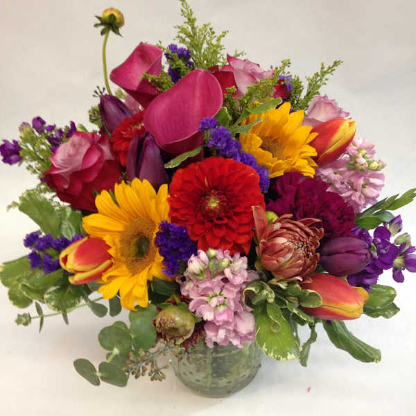 Mixed bouquet with sunflowers, tulips, roses, and calla lilies in a glass vase