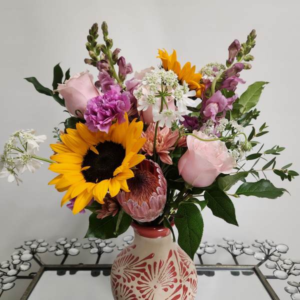 Mixed bouquet with sunflowers, pink roses, and purple blooms in a decorative vase