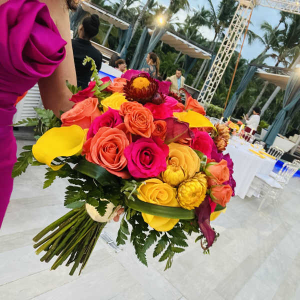 Bright bouquet of roses and calla lilies held at an outdoor event.