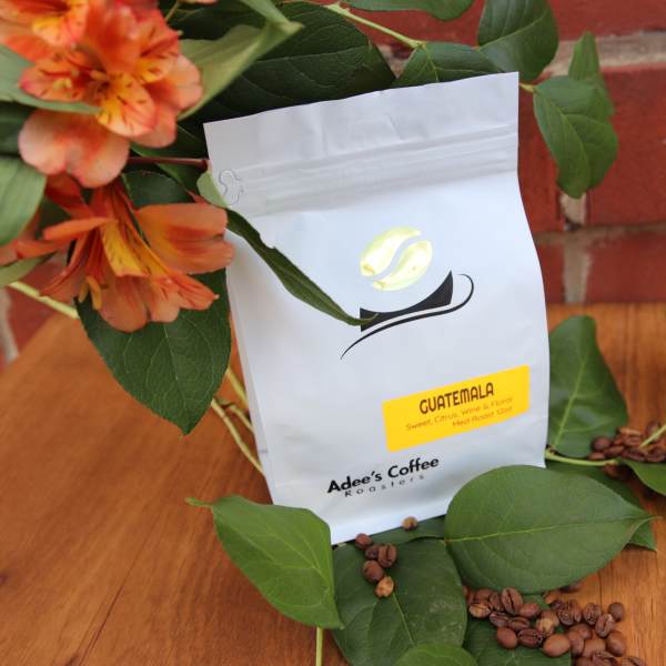 Coffee bag with orange flowers and scattered beans on a wooden surface