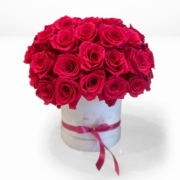 Round bouquet of red roses in a white hat box with a pink ribbon