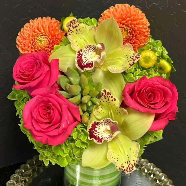 Pink roses and green orchids arranged with orange dahlias in a glass vase.