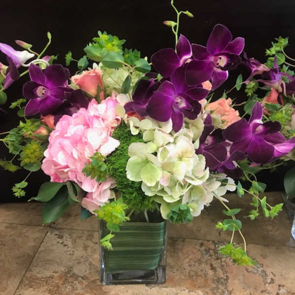 Purple orchids and pink hydrangeas in a square glass vase