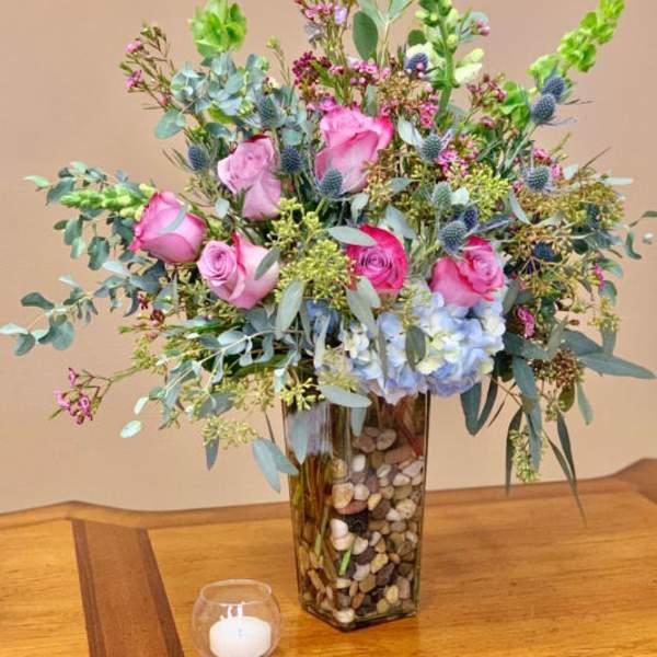 Pink roses and blue hydrangea in a tall glass vase with pebbles