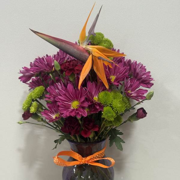 Purple and green bouquet with orange bird-of-paradise in a glass vase