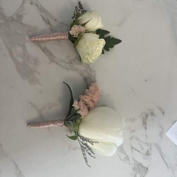 Two white rose boutonnieres with pink accents on a marble surface