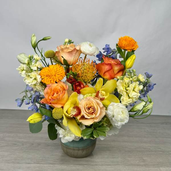 Mixed bouquet of orange, yellow, white, and blue flowers in a ceramic vase