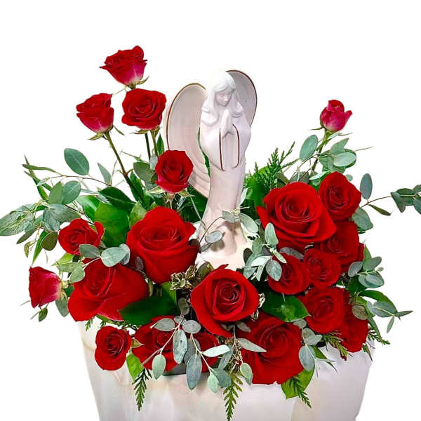 Red roses arranged around a white angel figurine in a vase.