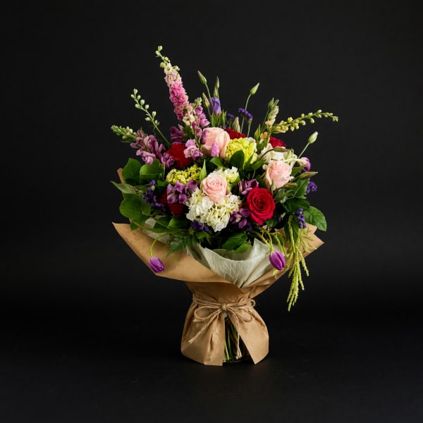 Mixed bouquet of roses, hydrangeas, and purple blooms wrapped in brown paper