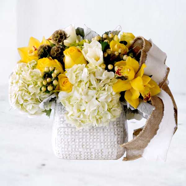 Yellow and white flower arrangement in a white textured vase with burlap ribbon