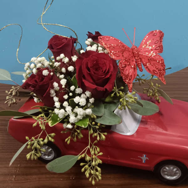 Red roses and baby's breath arranged on a red toy car with a pink butterfly