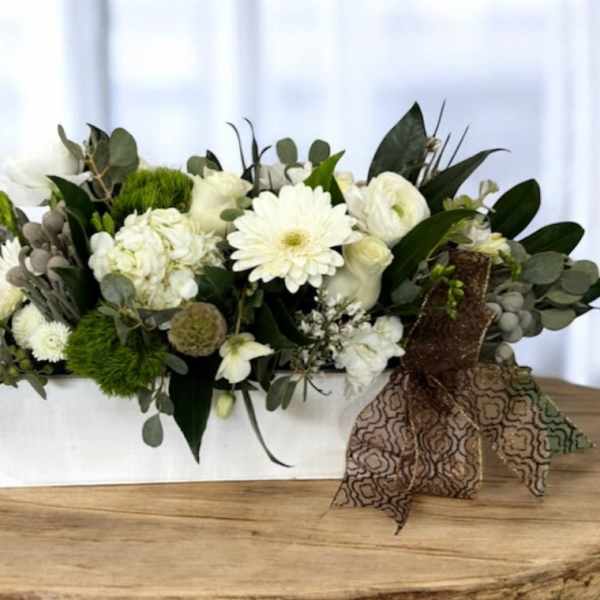 White floral arrangement in a rectangular white container with a patterned ribbon