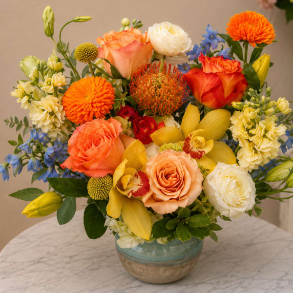 Mixed bouquet of orange, yellow, white, and blue flowers in a ceramic vase