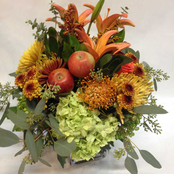 Orange lilies and chrysanthemums with apples in a glass vase