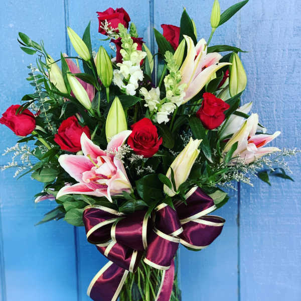 Bouquet of red roses and pink lilies in a clear glass vase with a purple ribbon