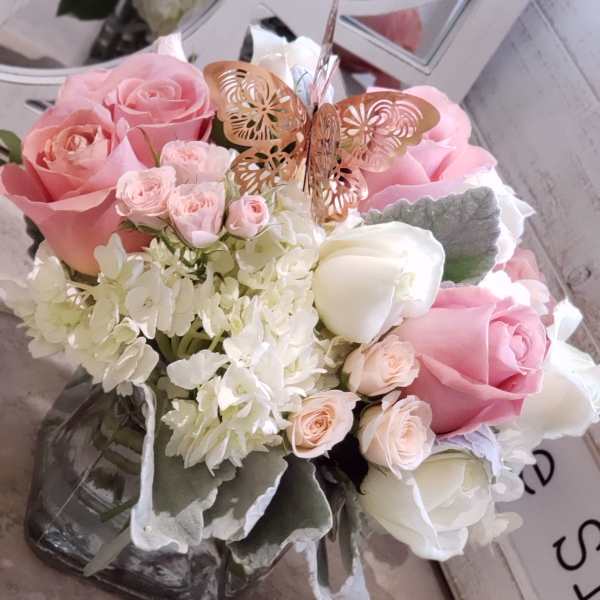Pink and white rose bouquet in a glass vase with a butterfly pick
